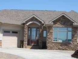 Tan-colored house with stone accents, a garage, and a driveway, under a clear blue sky.