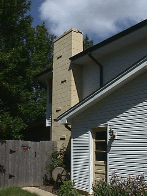 Brick chimney rising above a light blue siding house, wooden fence in foreground.