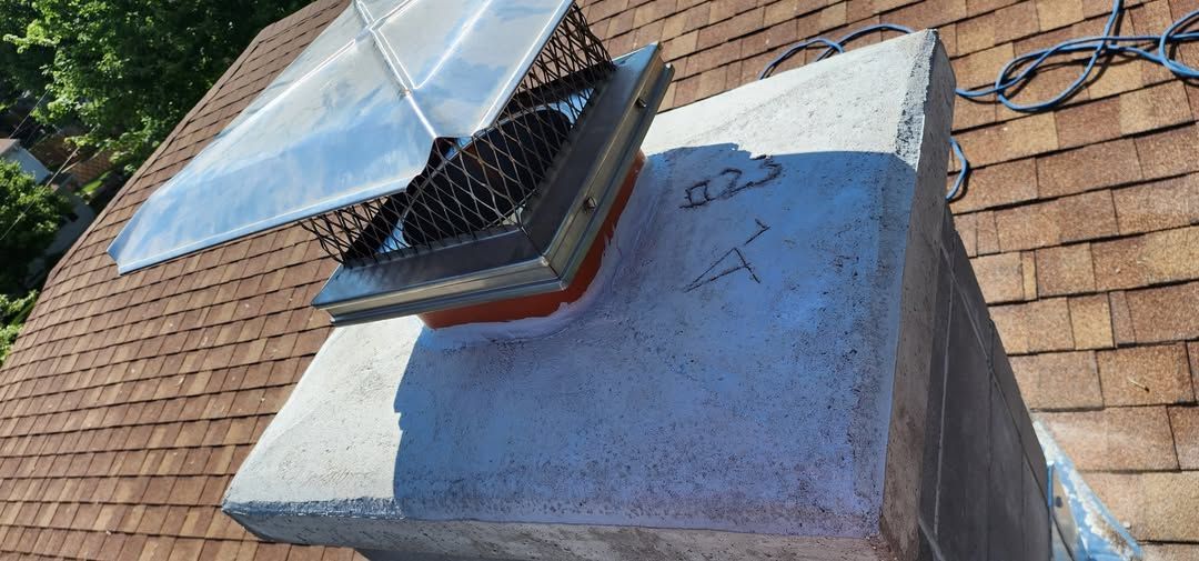 Chimney with a metal mesh cover on a brown shingled roof. Handwritten numbers on the chimney.