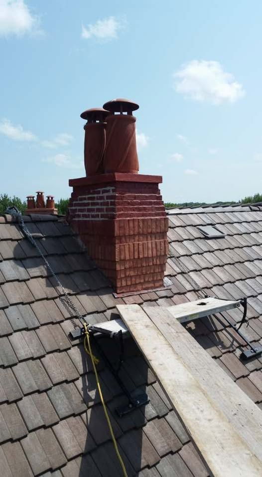 Brick chimney with two metal caps on a tiled roof under a blue sky.