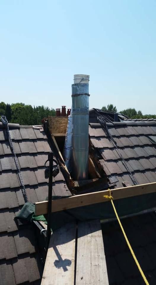 Chimney on a roof being worked on, with wooden support beams and a metal flue extending upwards.