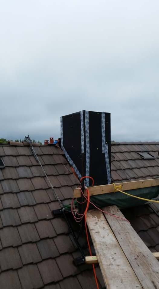 Chimney wrapped in black material on a brown tiled roof under a cloudy sky.
