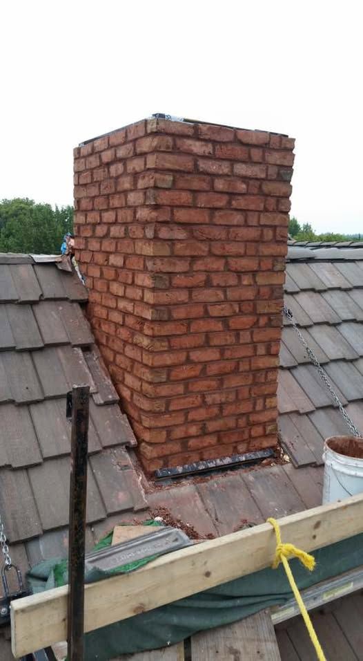 Brick chimney on a tiled roof. The chimney is rectangular and freshly constructed with red bricks.