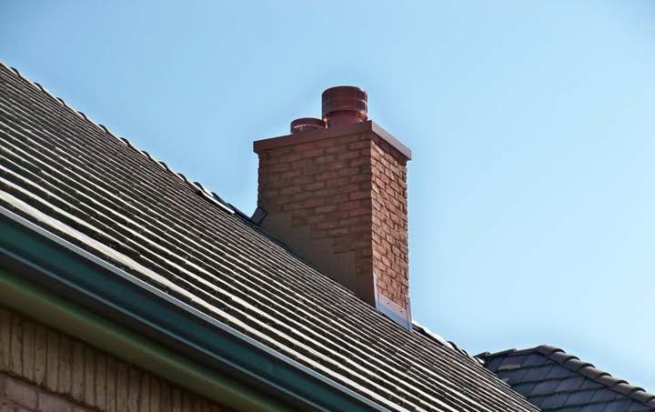 Brick chimney on a gray-roofed house against a clear, blue sky.