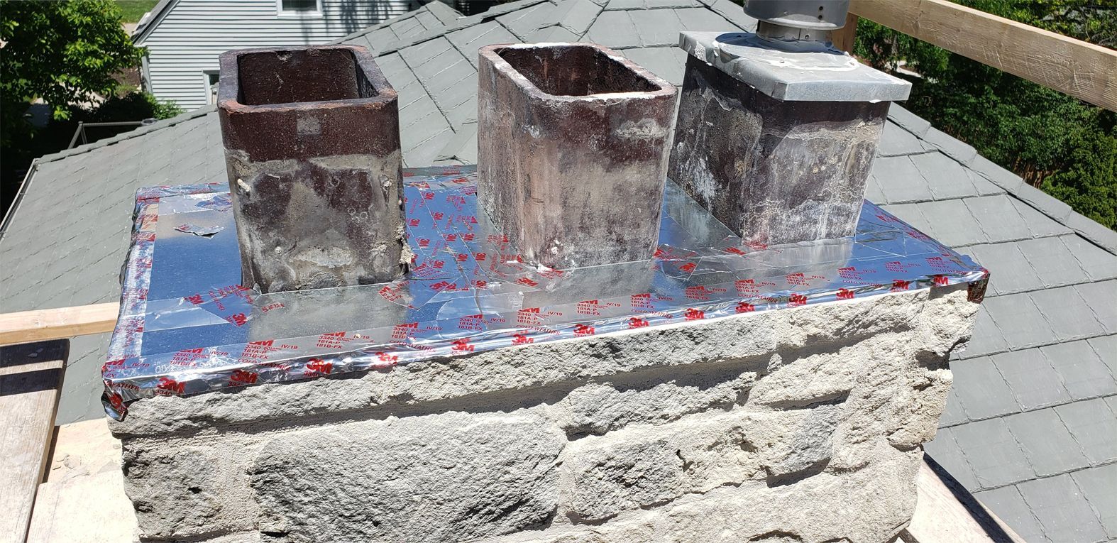 Chimney with three flues and a metal cap on a gray rooftop.