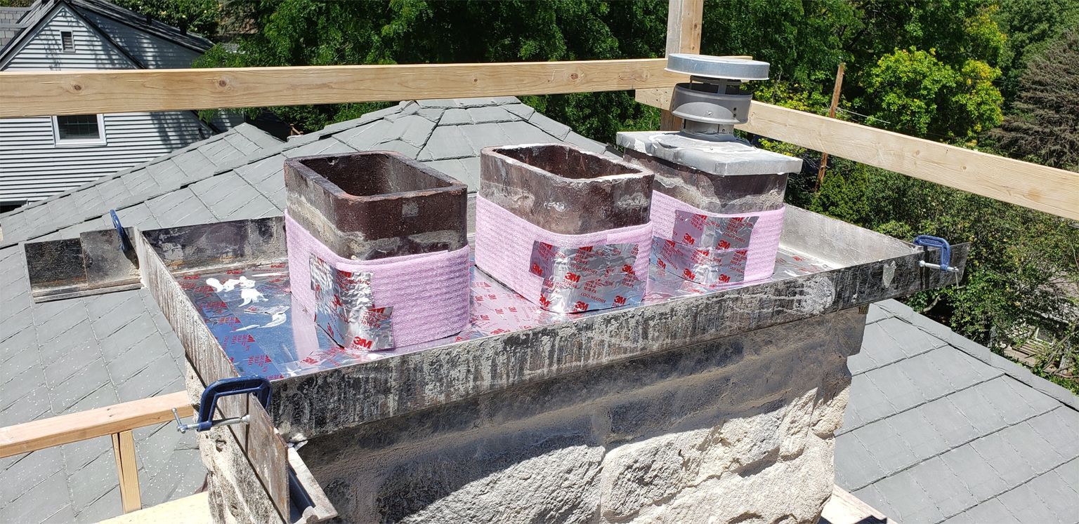 A chimney under construction on a rooftop, with pink foam insulation visible.
