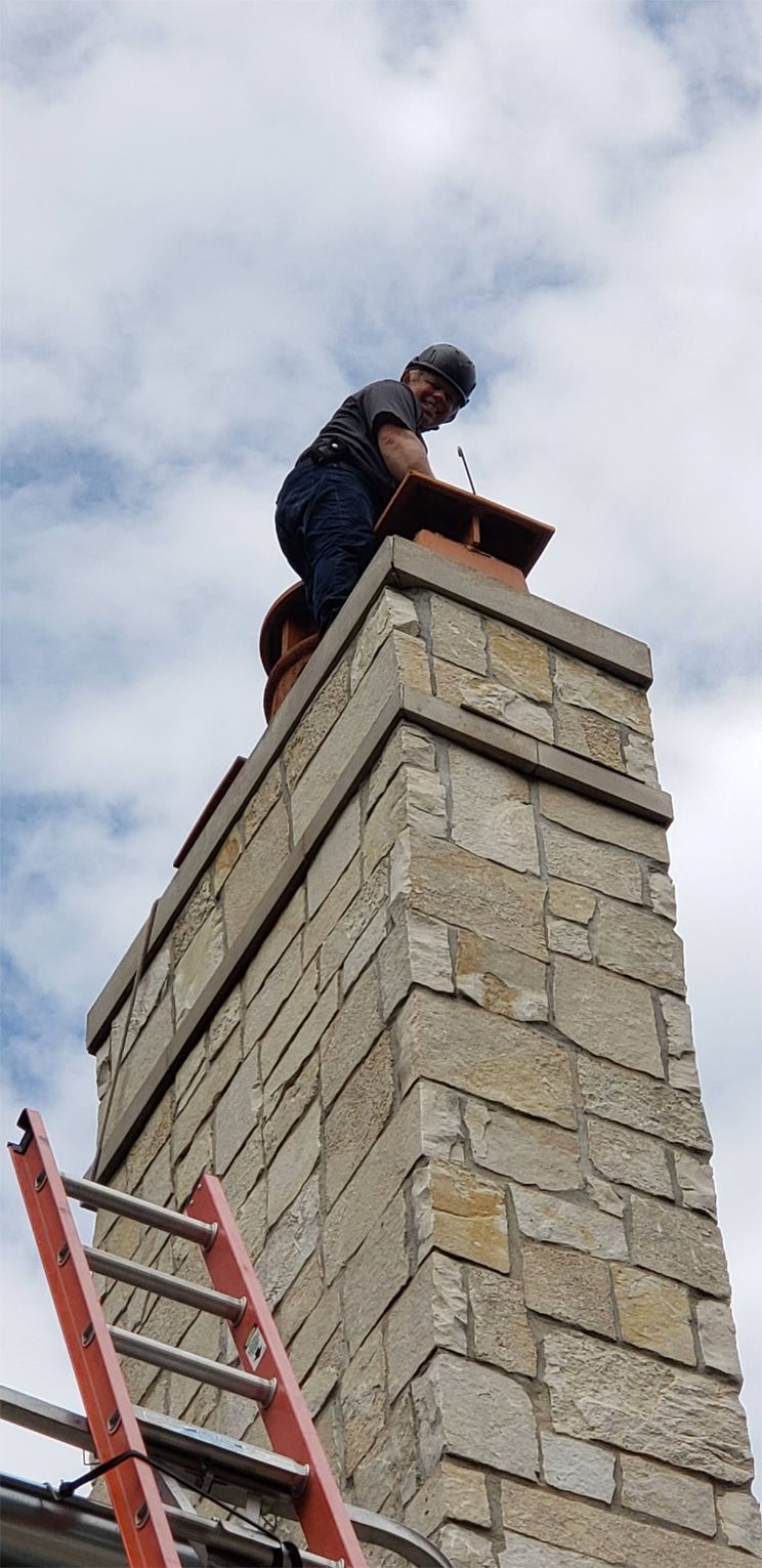 Person on a chimney inspecting the flue. Red ladder leans against the stone structure. Overcast sky.
