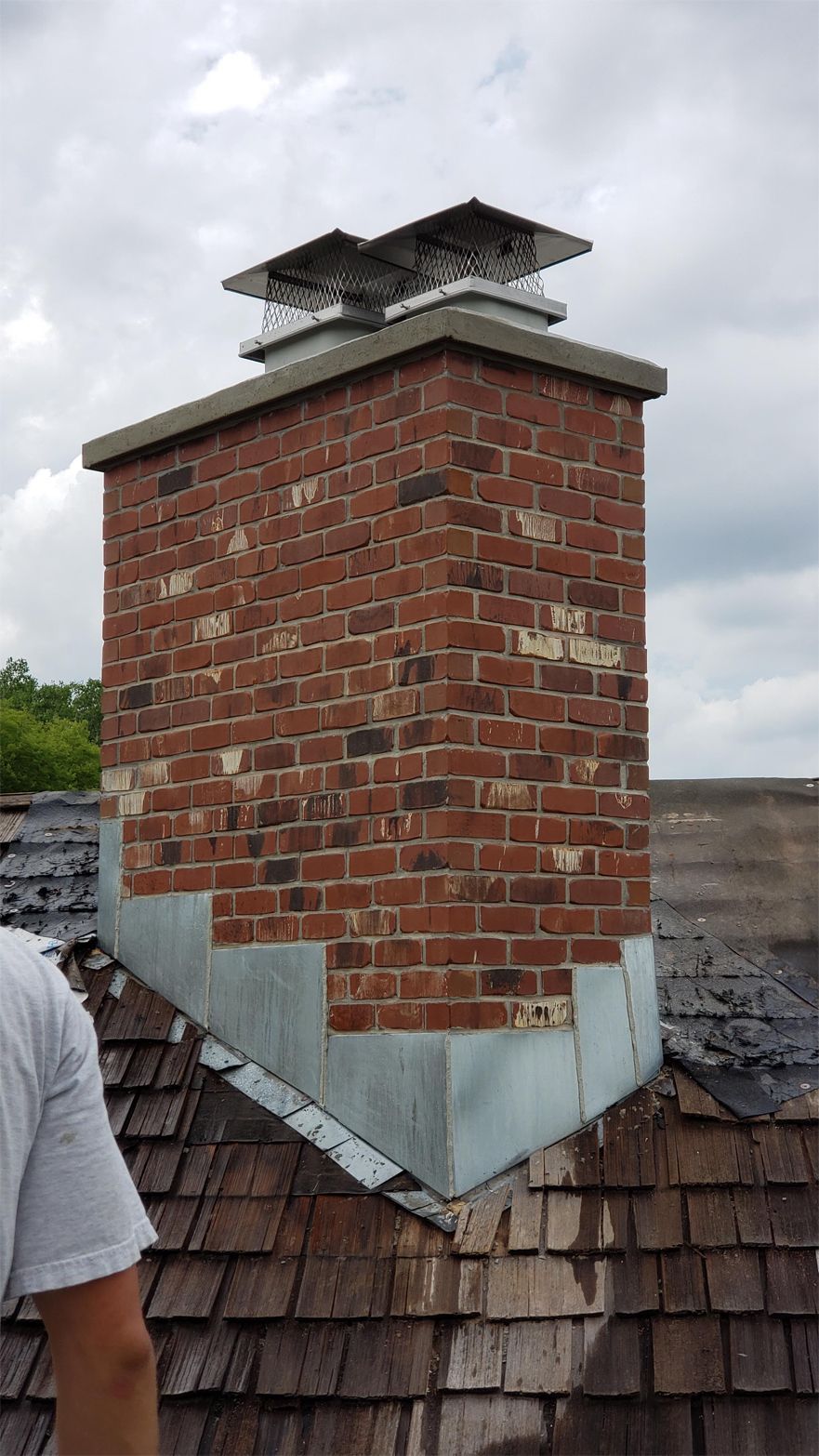 Brick chimney with a metal cap on a shingle roof.