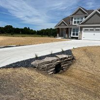 A large house with a concrete driveway and a stone wall in front of it.