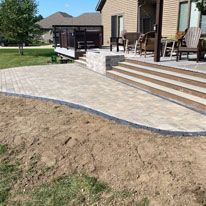 A patio with stairs and a deck in front of a house.