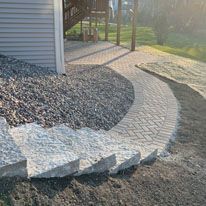 A brick walkway leading to a house next to a pile of gravel.