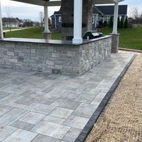 A patio with a stone bar and a grill under a pergola.