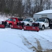 A row of snow plows parked in the snow in front of a building.