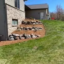 A house with a rock wall in front of it and a lush green lawn.