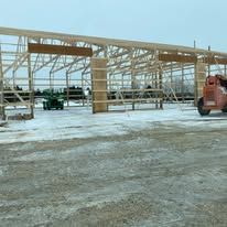 A man is driving a forklift in front of a building under construction.