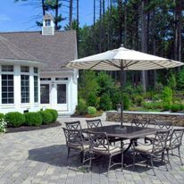 There is a table and chairs under an umbrella in front of a house.