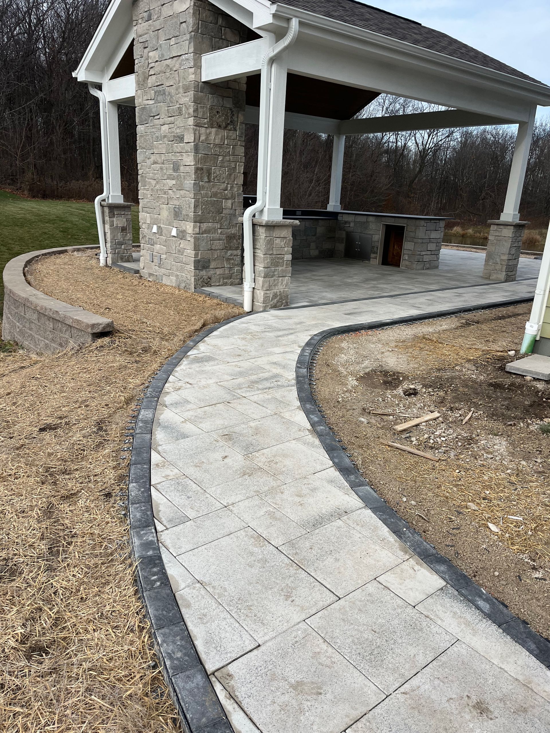 A walkway leading to a stone building with a pavilion in the background.