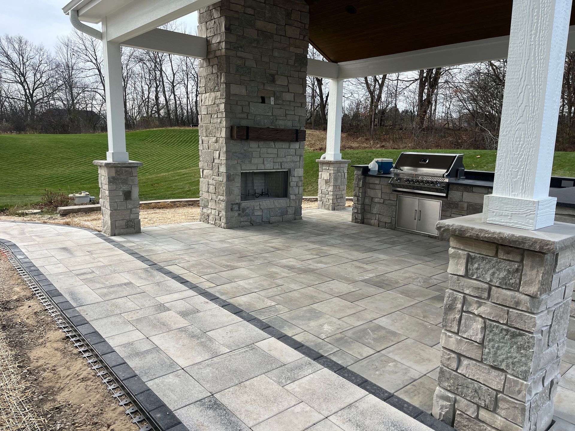A patio with a fireplace and a grill under a pavilion.