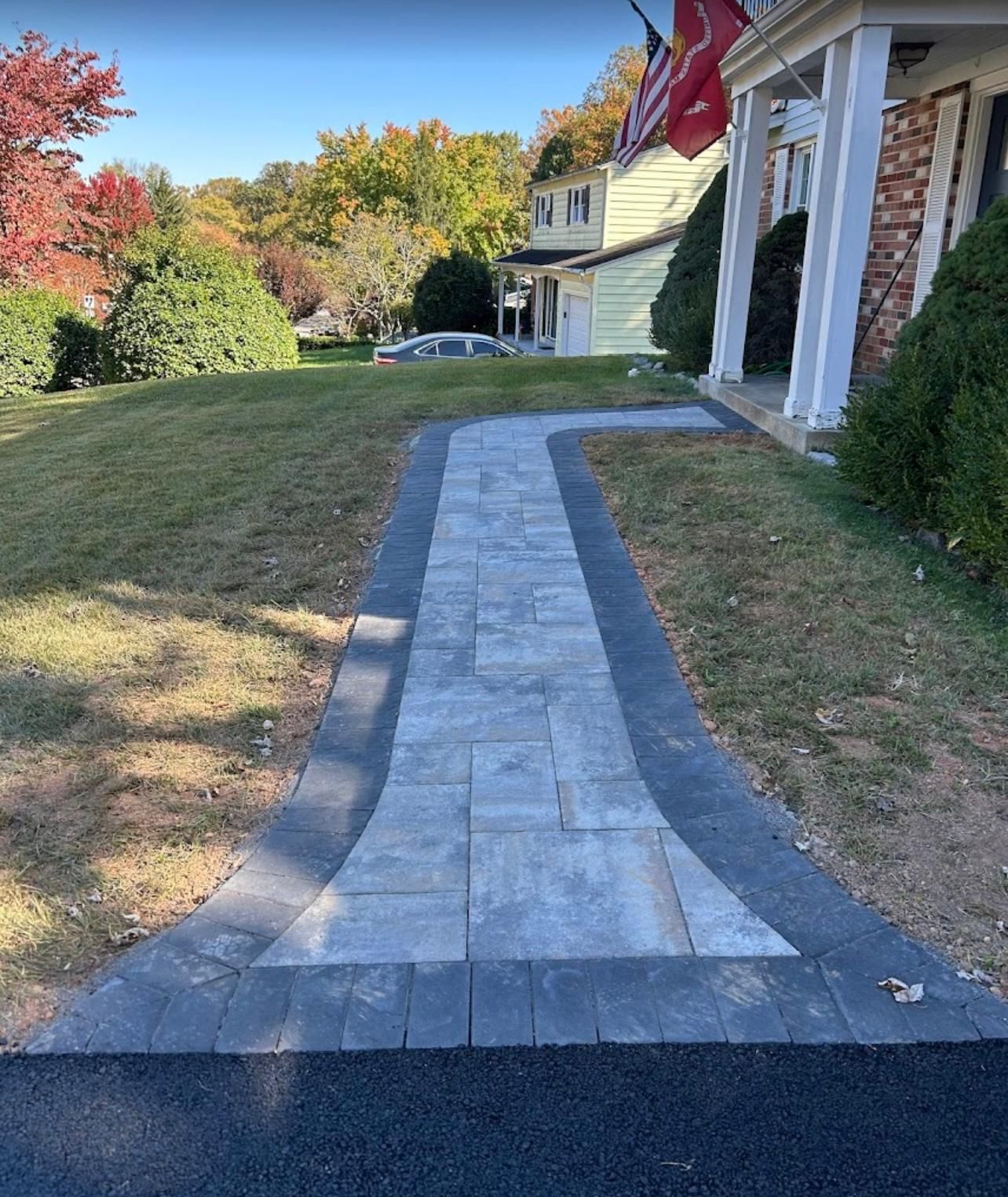 A brick walkway leading to a house with a flag on the side of it.