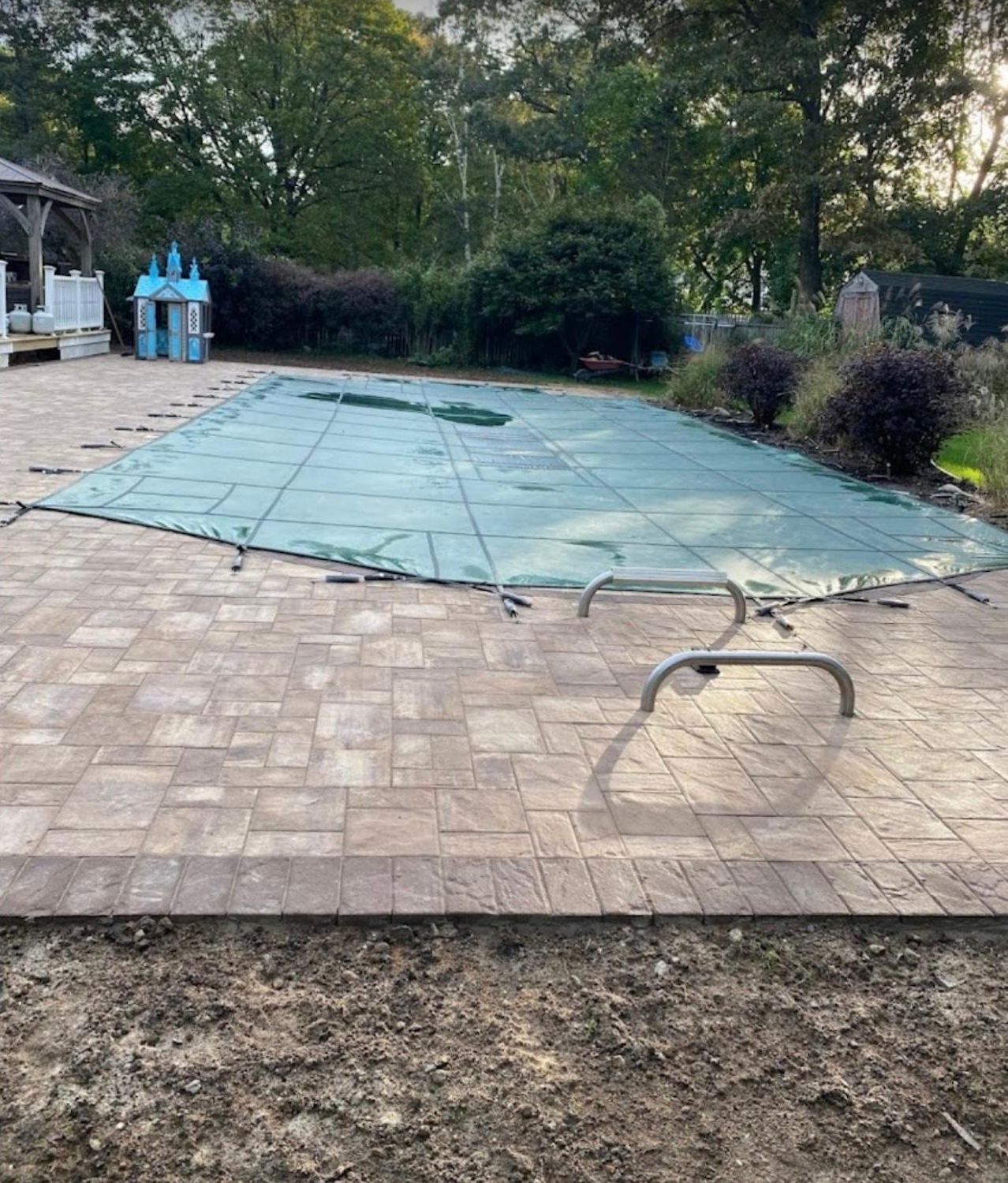 A pool with a cover on it is sitting on top of a brick patio.