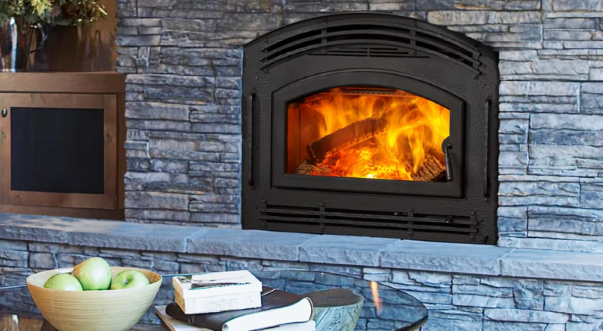 Technician in orange sweater installing a black fireplace insert in a white room