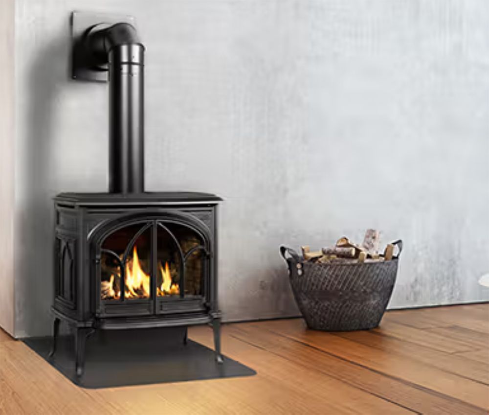 Black wood stove with fire burning beside a basket of firewood on a wooden floor.