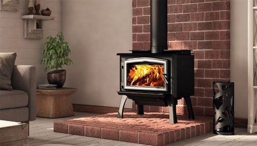 Wood-burning stove with a bright fire in a cozy living room beside a brick hearth and potted plant.