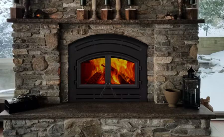 Stone fireplace with a burning fire and black arched insert on a rustic hearth