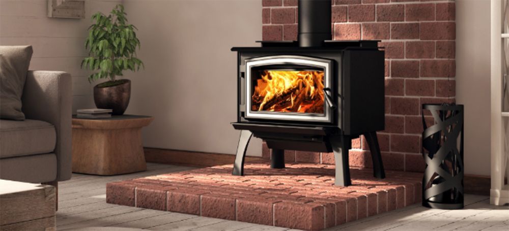 A lit wood stove in a brick fireplace with a tan sofa and potted plant nearby.