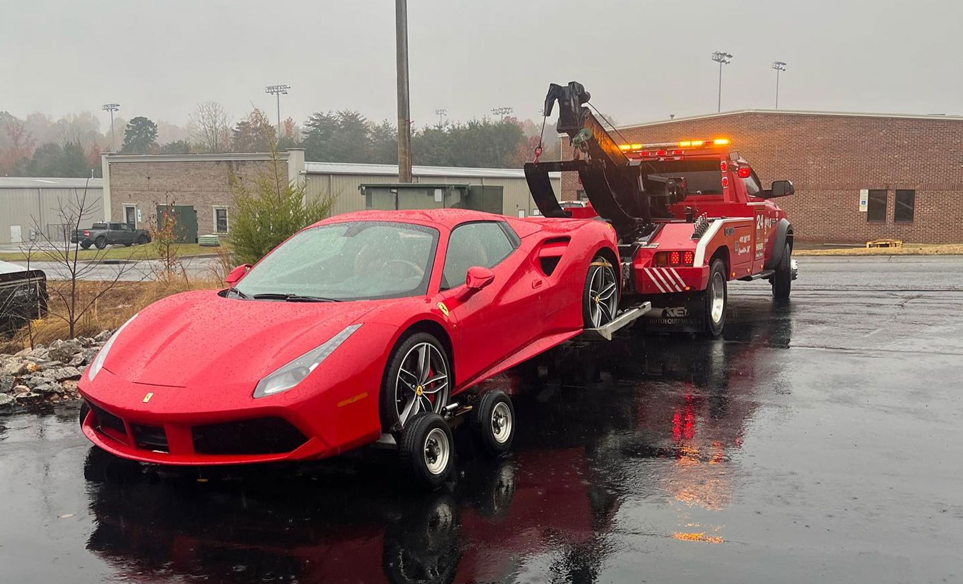 Red Ferrari being towed by a red tow truck on a rainy day.