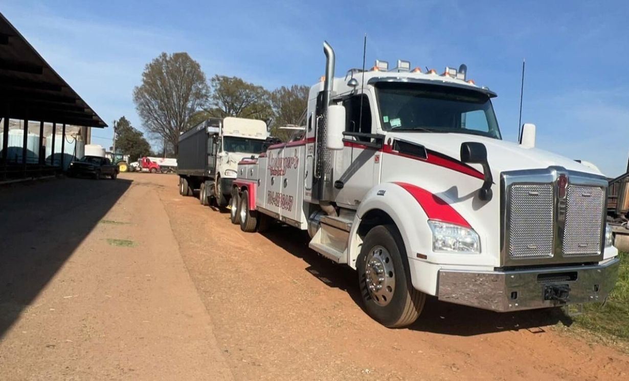 A white tow truck with red accents towing a smaller truck on a dirt road.
