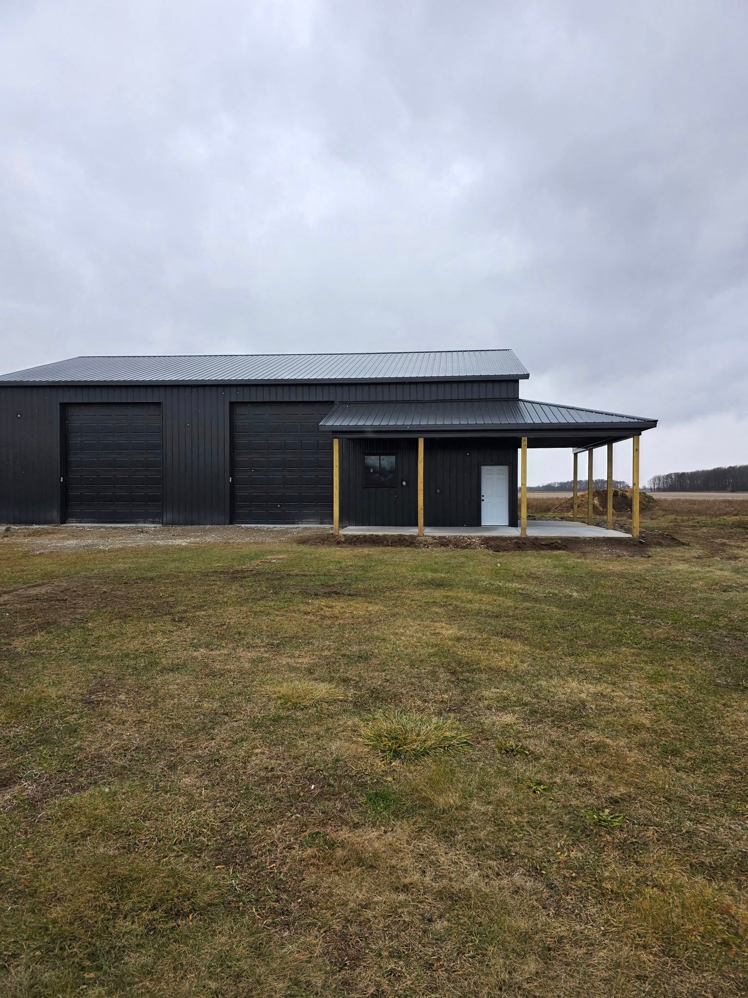 Dark gray barn with attached covered porch on a cloudy day; green and brown grass in foreground.