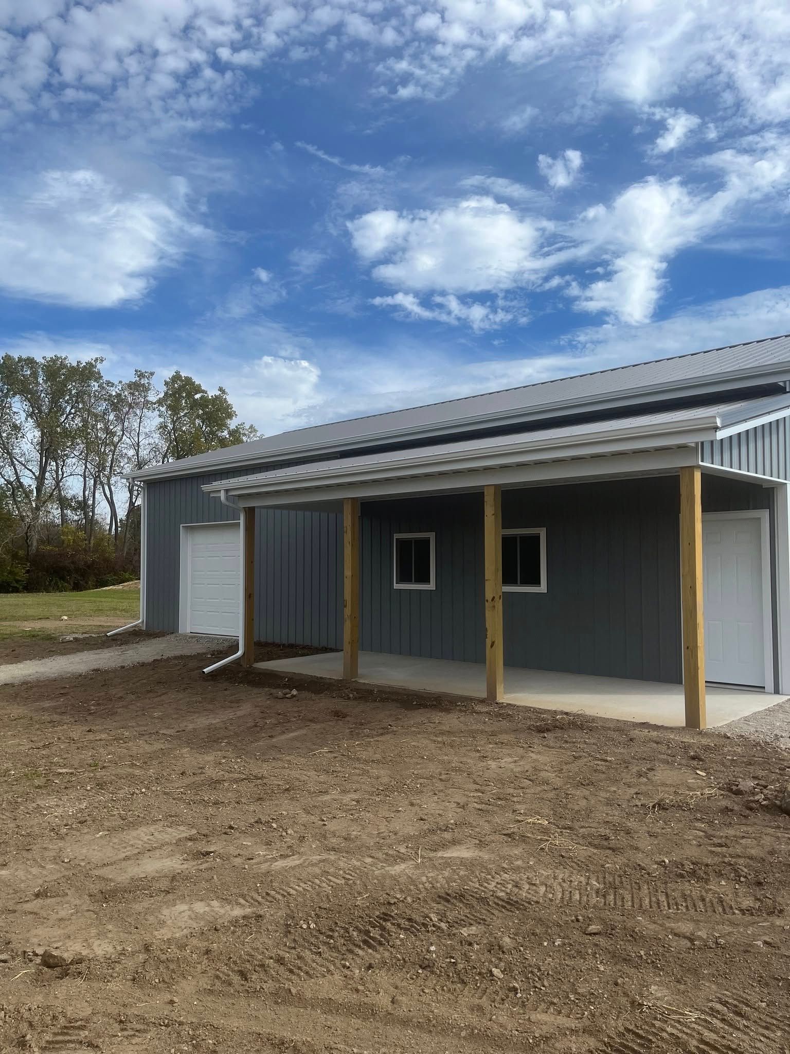 Gray metal building with porch and white trim under a cloudy sky.