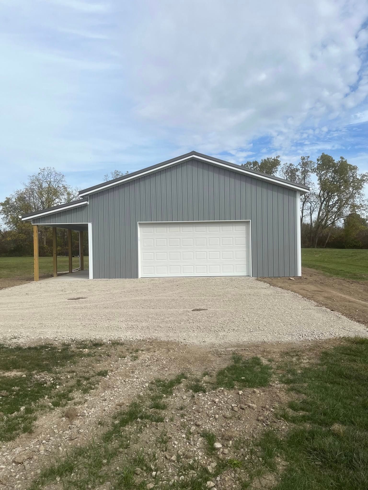 Gray metal garage with white garage door and gravel driveway.