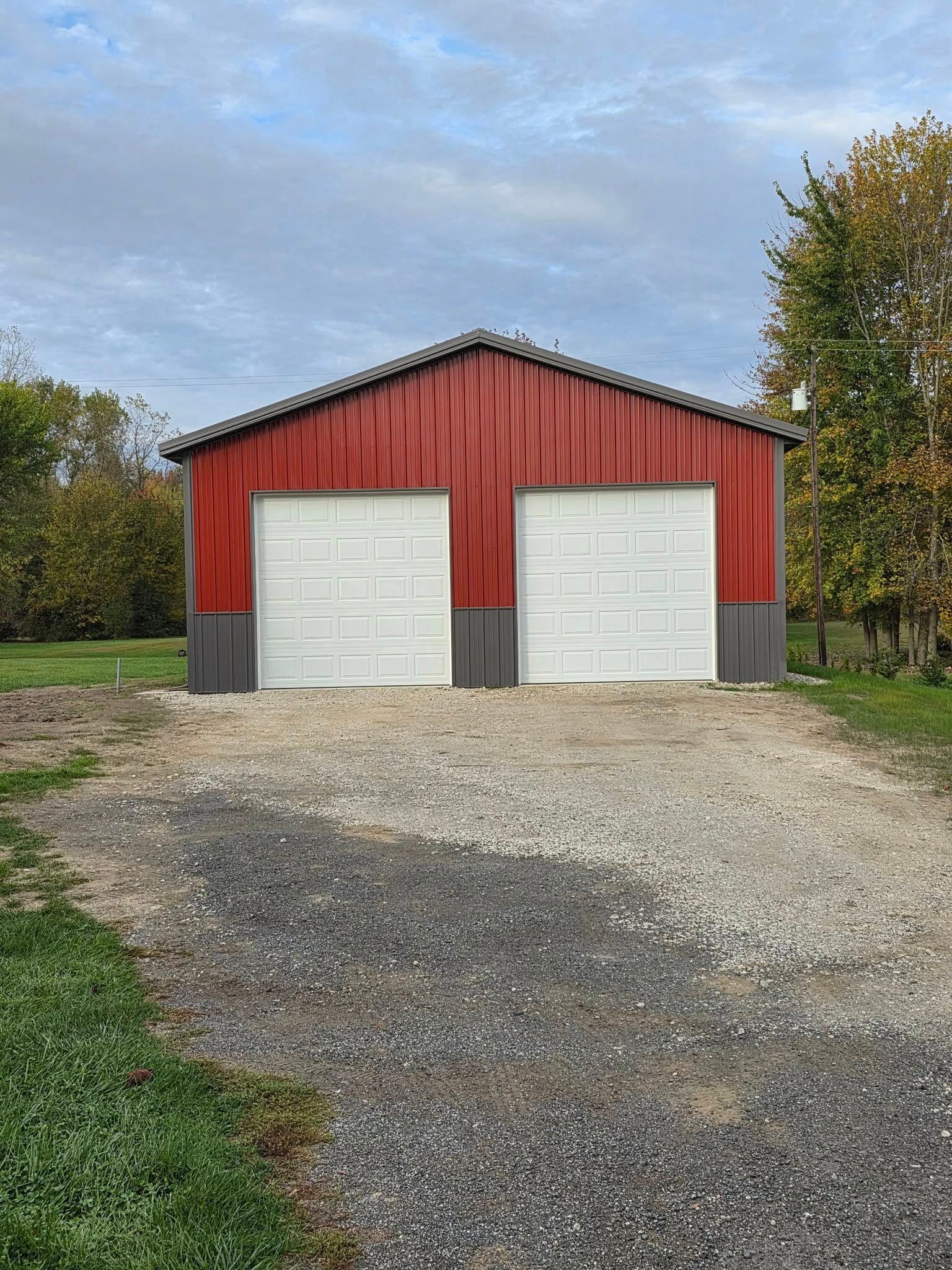Red two-car garage with white doors on a gravel driveway, against a cloudy sky.