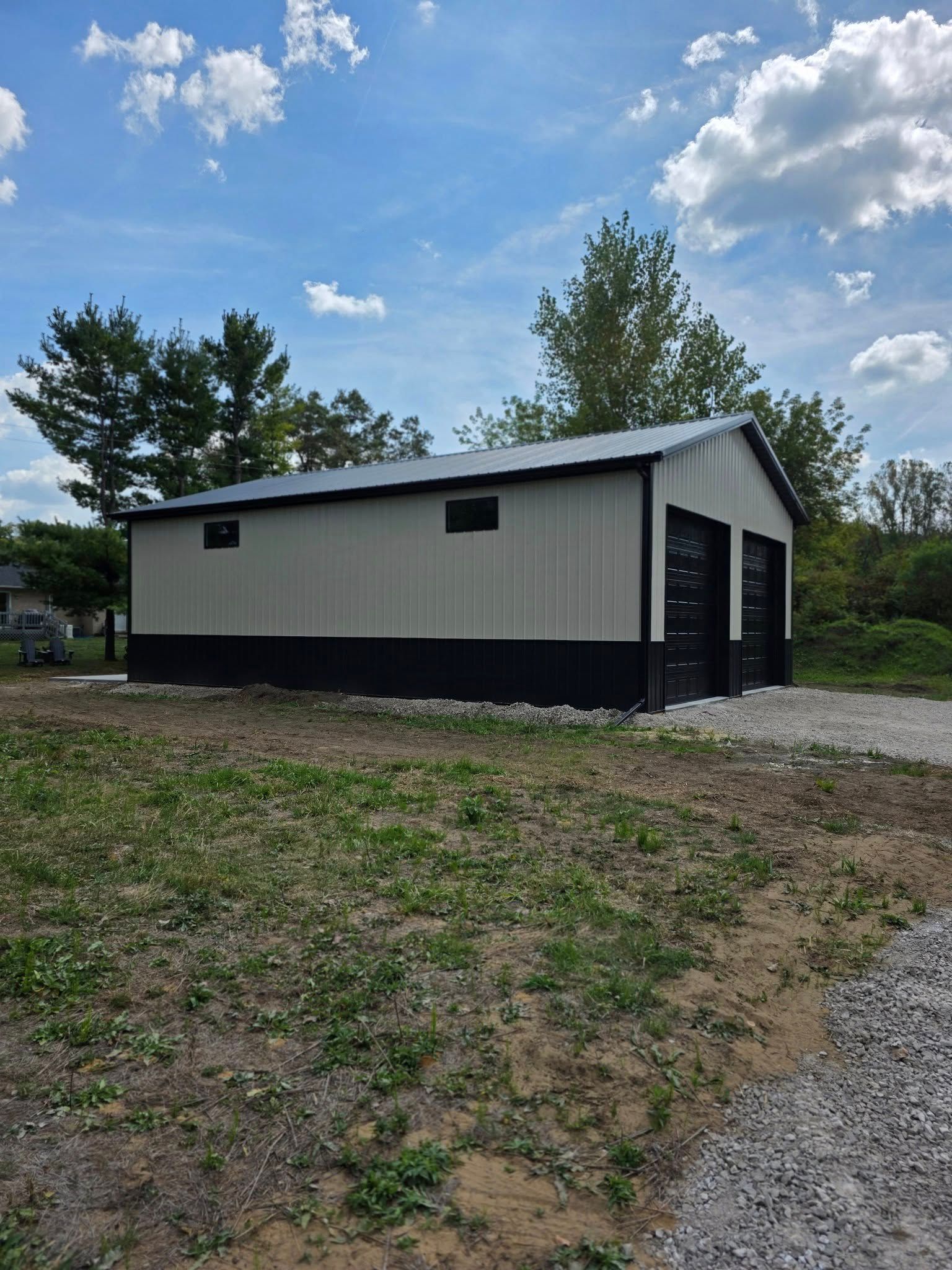 Metal garage with black doors and trim, beige walls, and a black roof, on a gravel driveway.