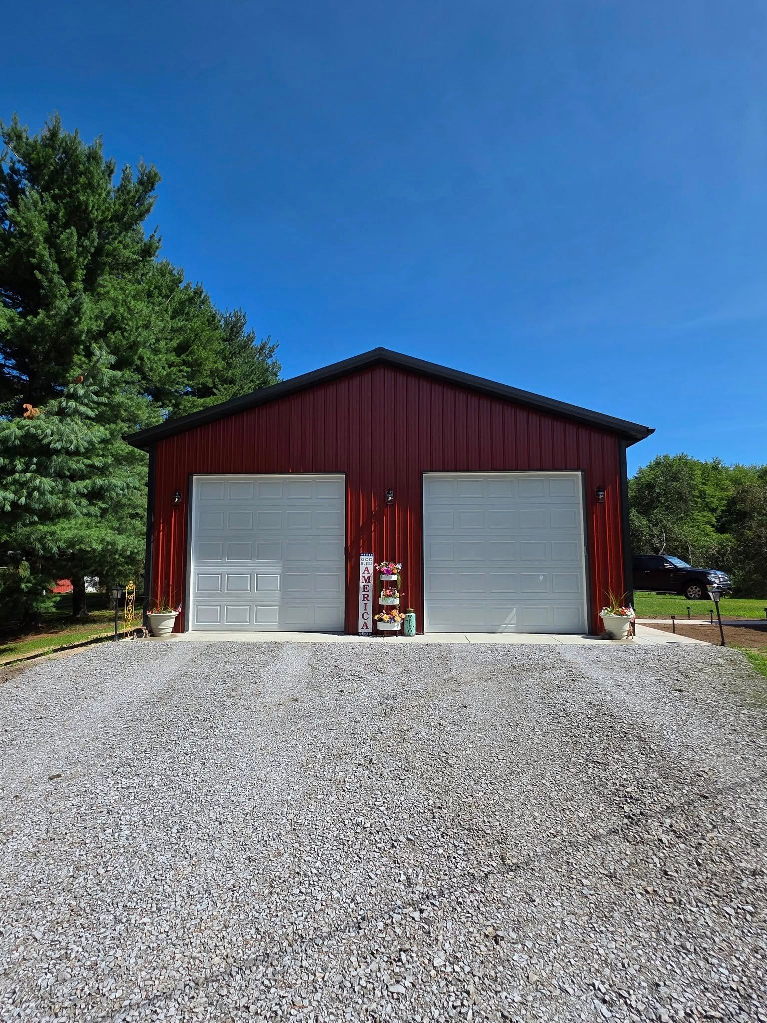 Red metal garage with two gray garage doors on a gravel driveway, under a clear blue sky.