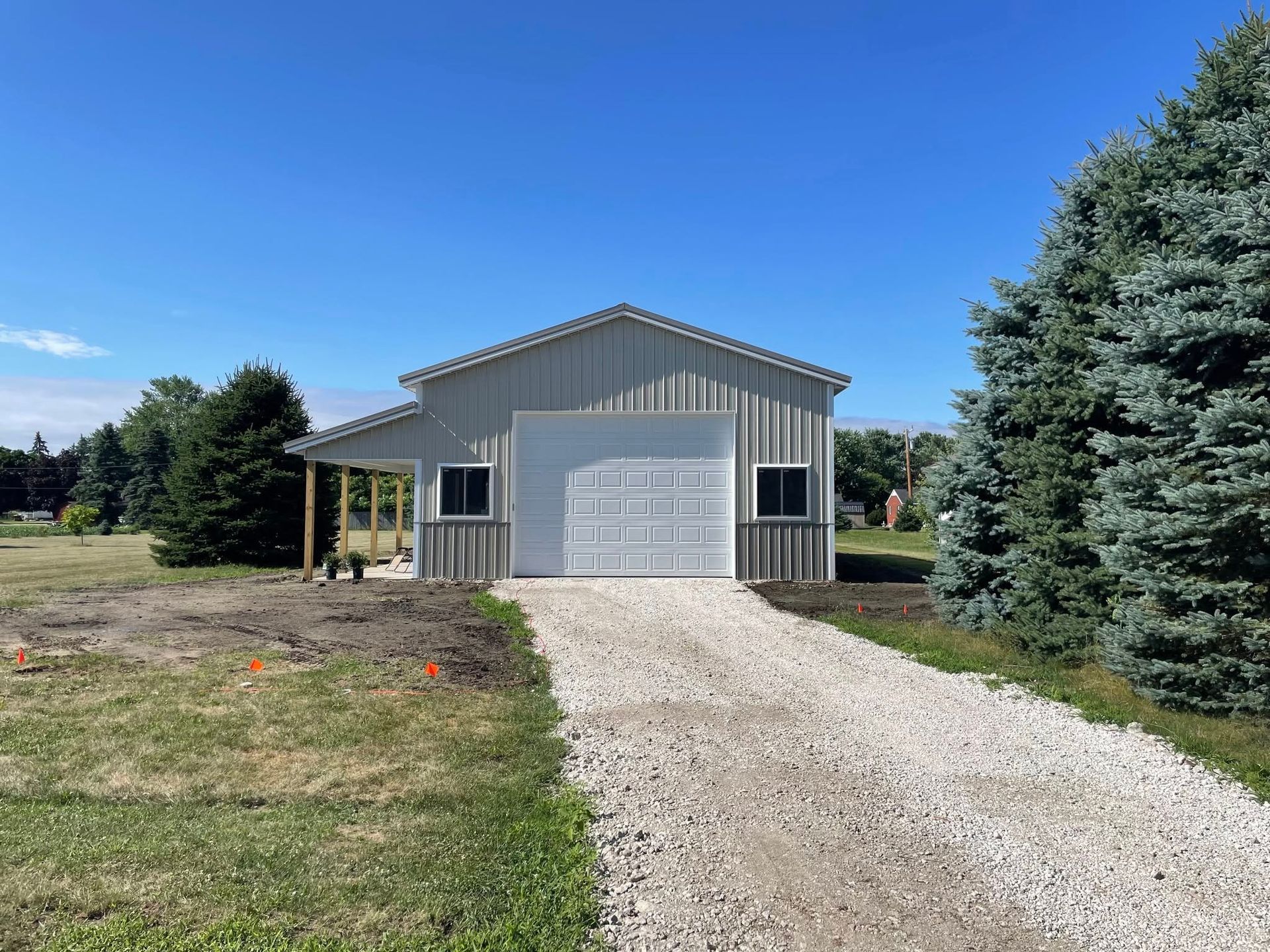 Gray metal garage with white garage door and gravel driveway, under a blue sky.