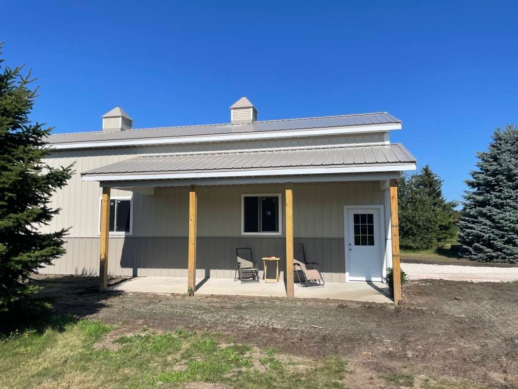Tan and gray building with a porch, chairs, and door under a blue sky.