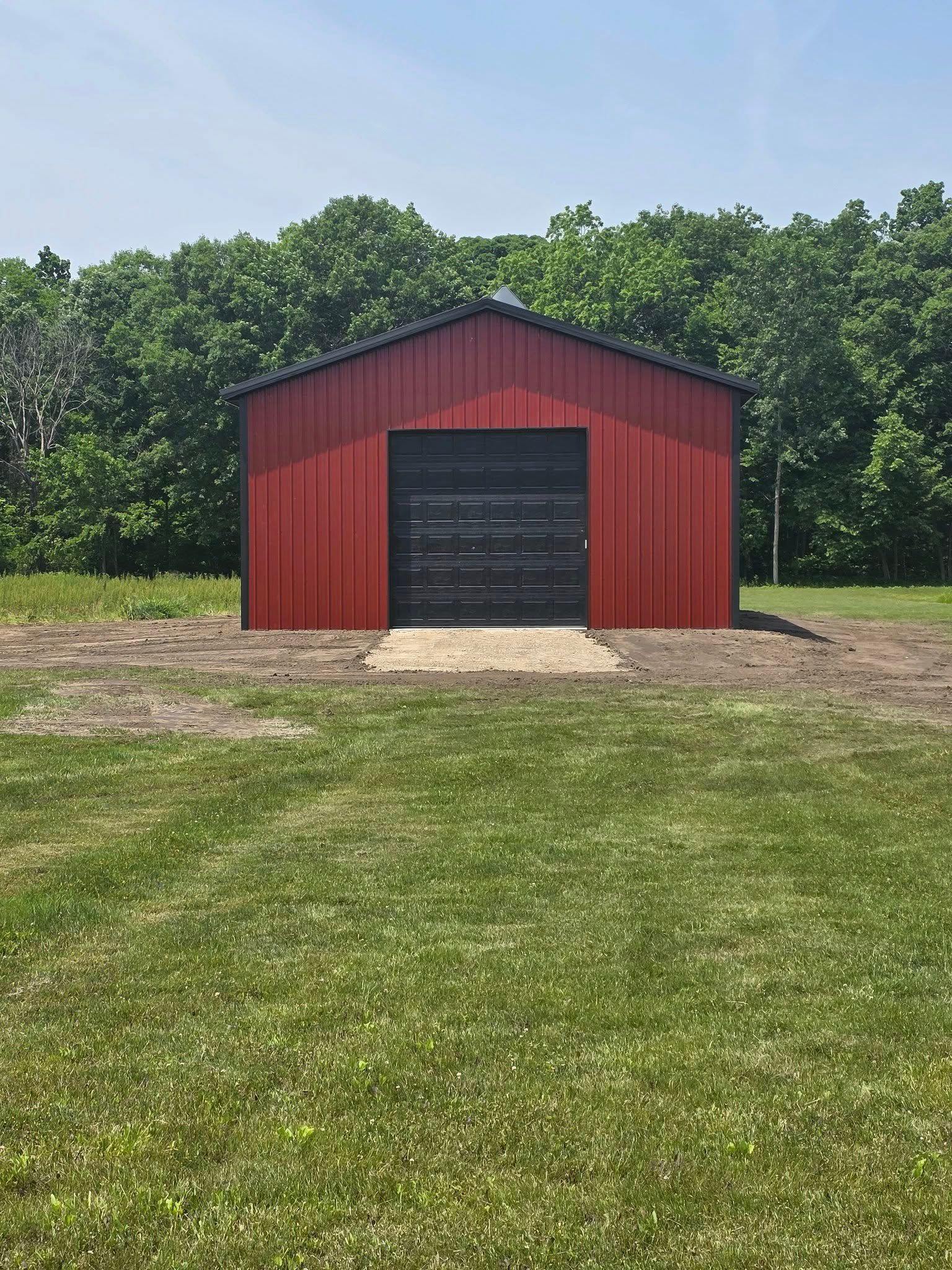 Red metal shed with black door, set in grassy yard against a backdrop of trees.