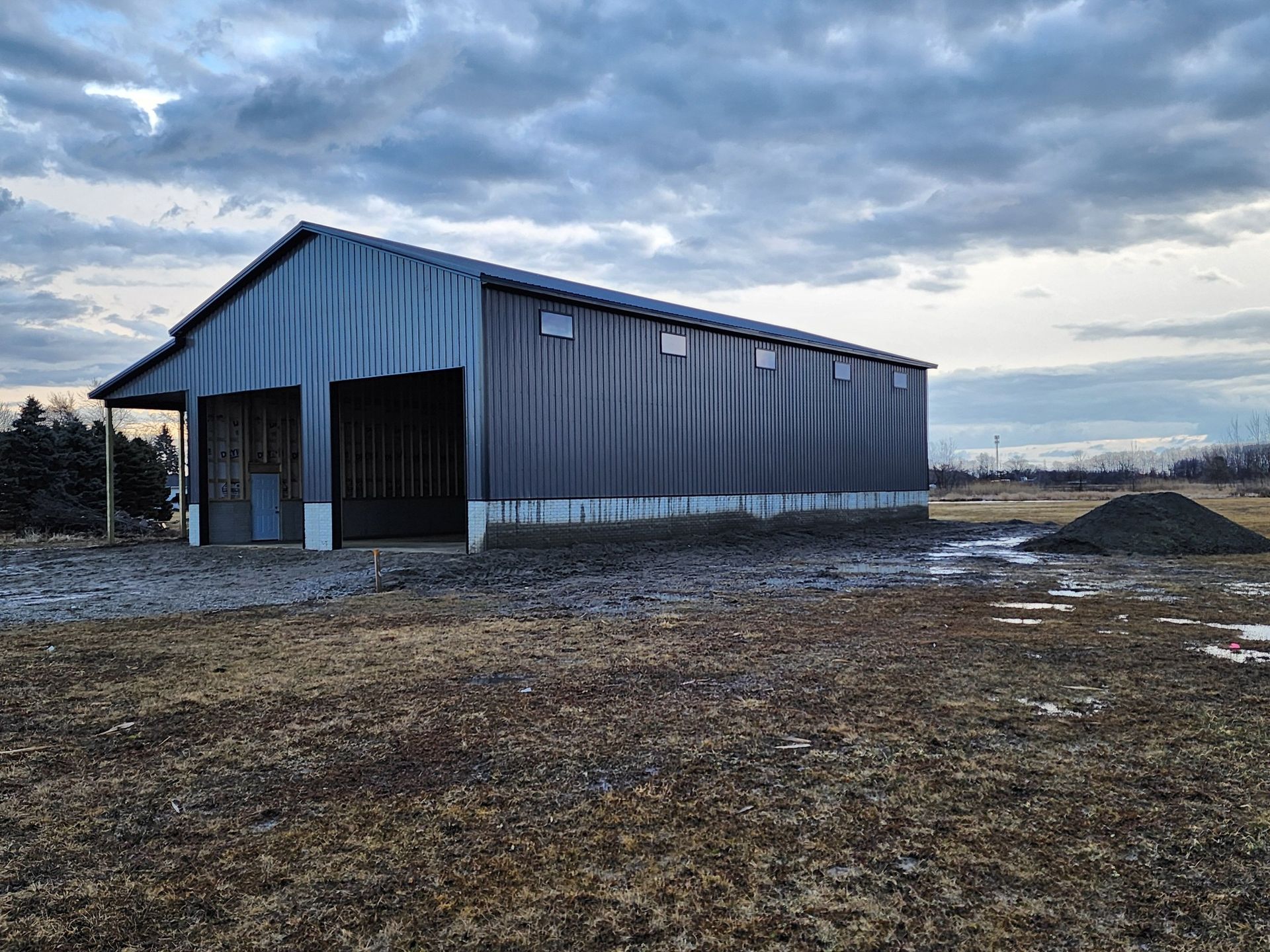 Metal barn under a cloudy sky, sitting on a brown field.