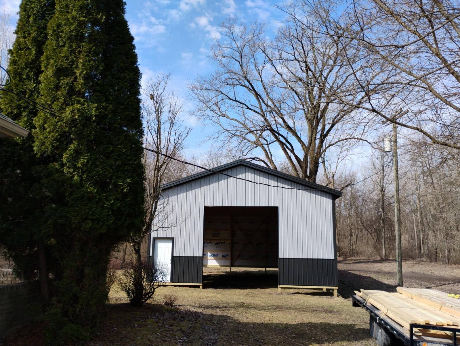 Metal barn with open front and black accents under a blue sky.