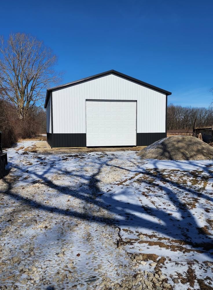 White and black barn on a sunny, snowy day. Garage door closed, trees in background.