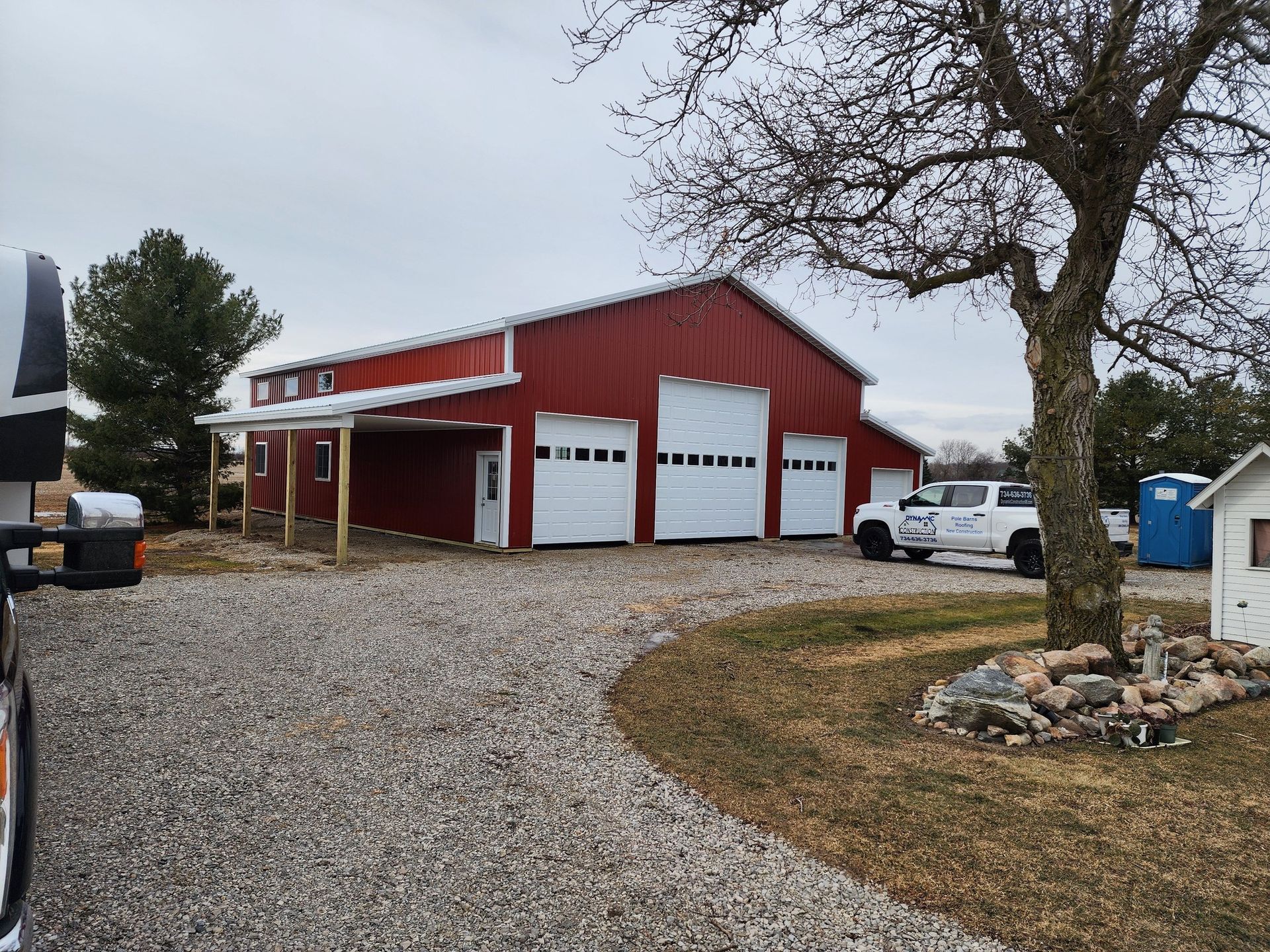 Red barn with white garage doors and a pickup truck parked on gravel.