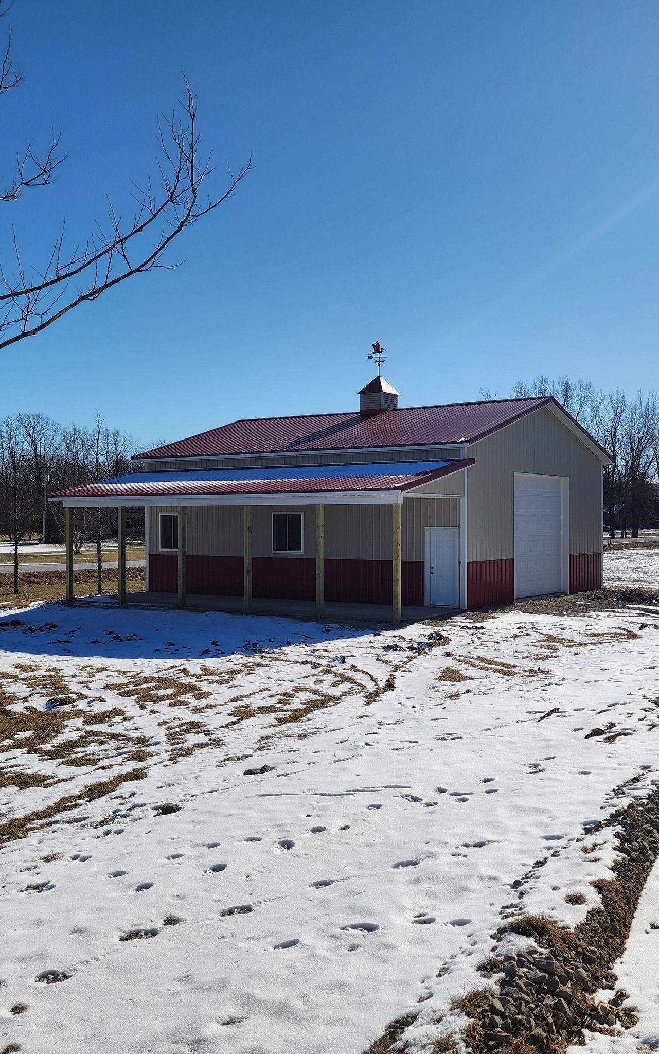 Barn with red roof and trim against a clear blue sky, partially covered in snow.