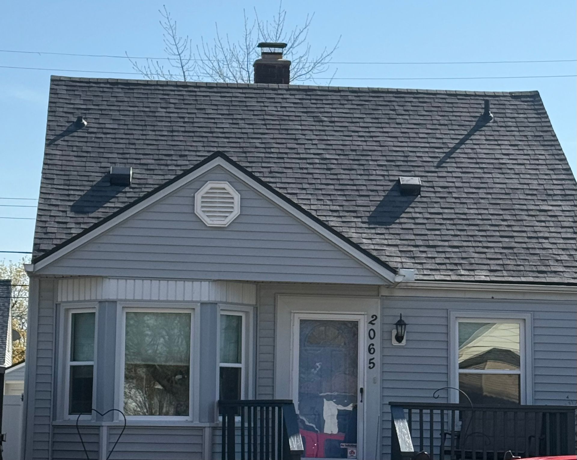 A light blue house with a gray roof. Features a bay window, front door, and chimney.