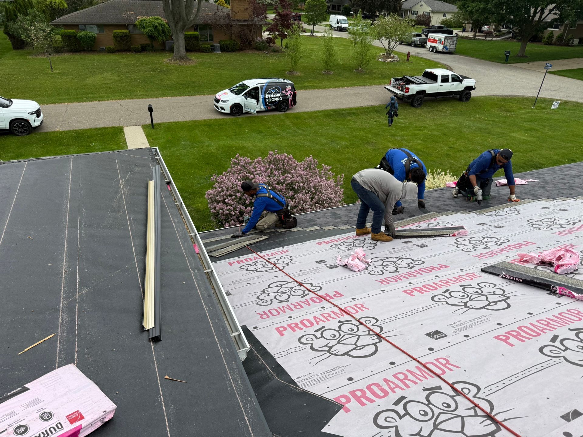 Roofers install shingles on a roof, green lawn in the background, sunny day.