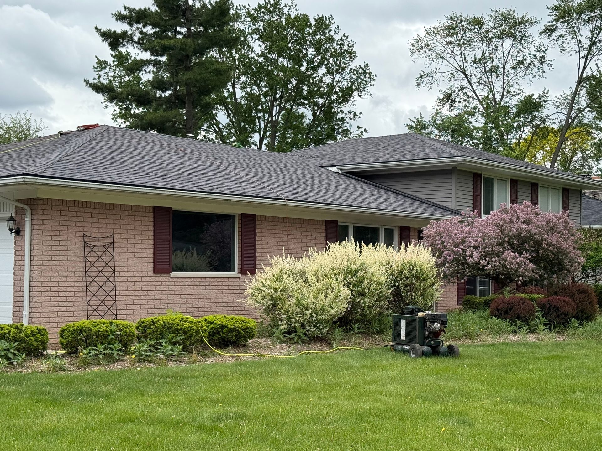 Brick house with dark roof, green lawn, and shrubs; a robotic lawnmower is in the foreground.
