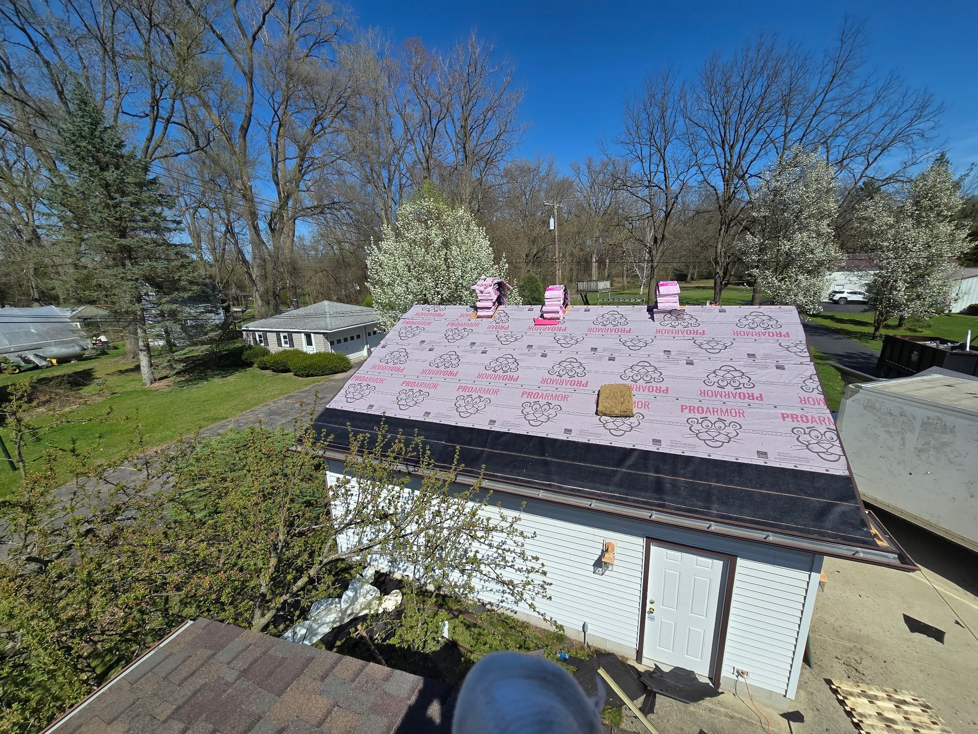 A partially roofed white garage with pink insulation, under a clear blue sky and trees.
