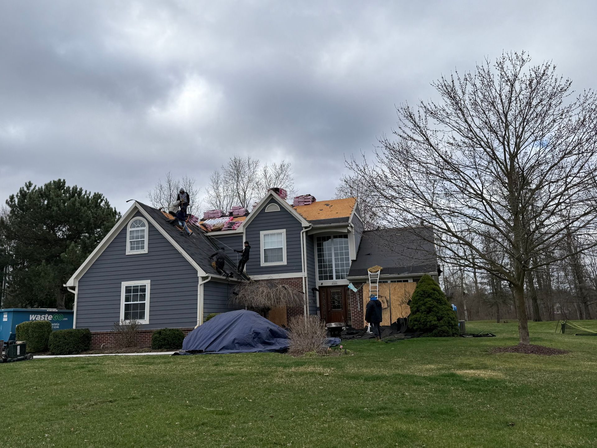 Roofers working on a house; part of roof removed and partially replaced, cloudy day.